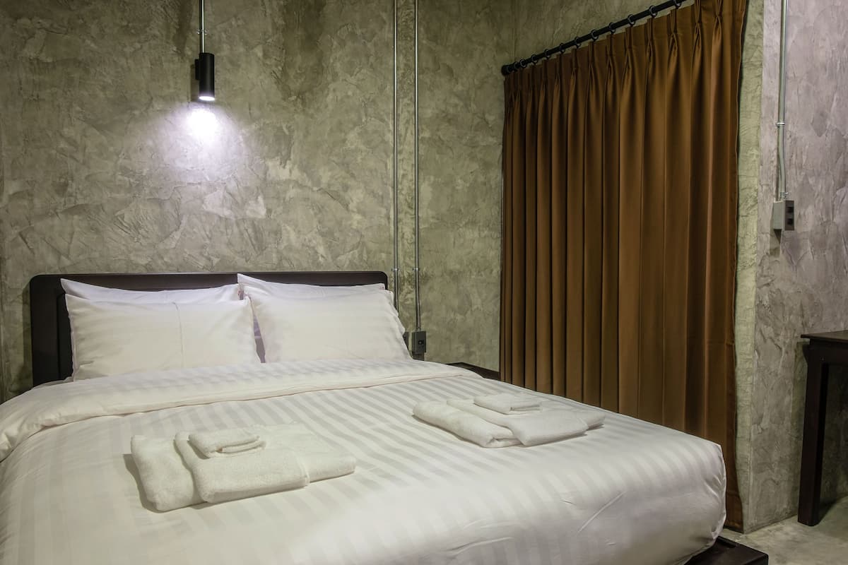 A neatly made bed with white linens and towels, a headboard, and a light fixture above it.