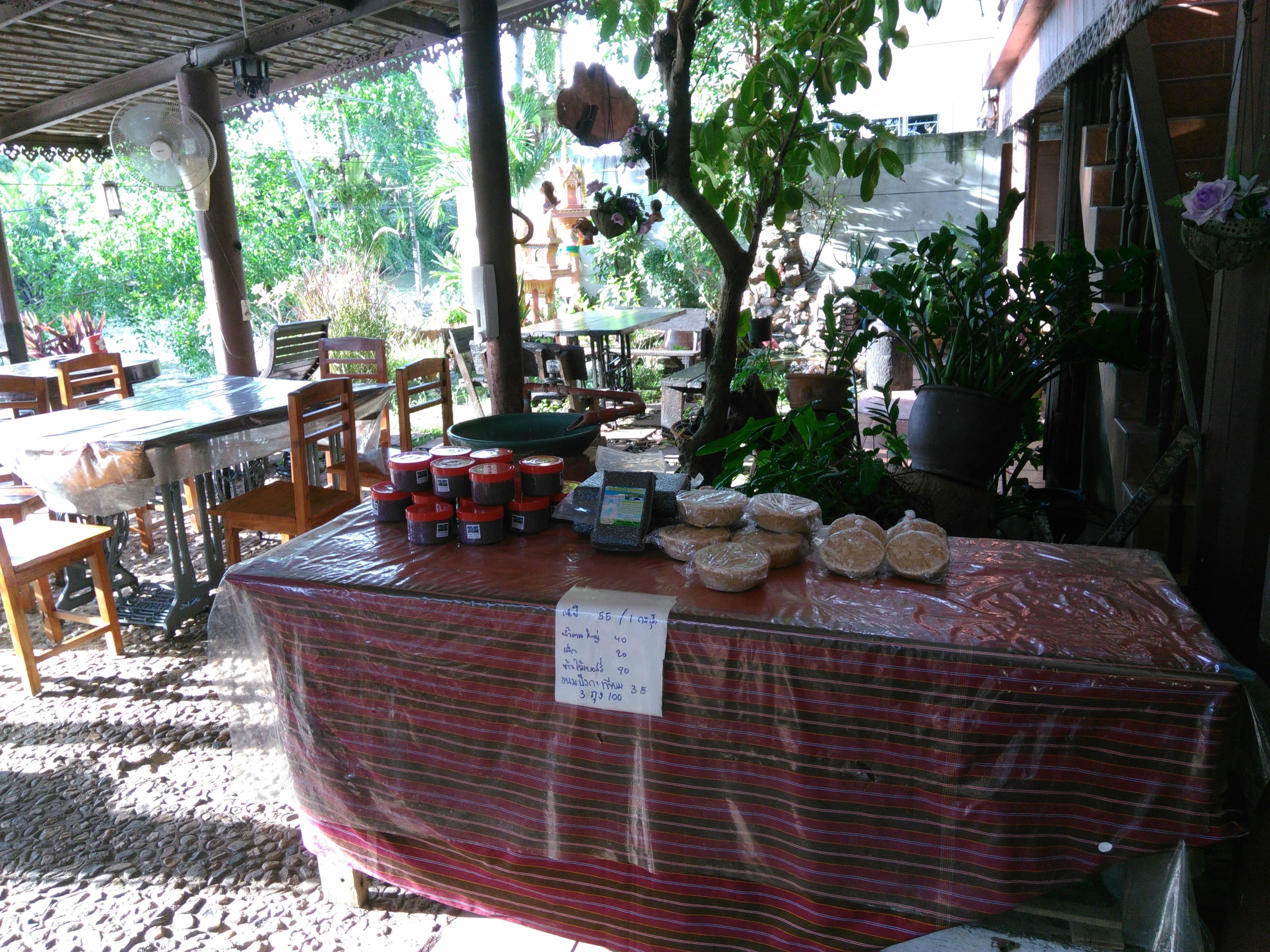 A covered outdoor market area with tables displaying food items and a sign listing prices.