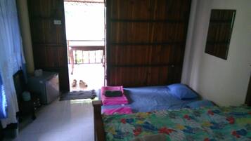 A room with a bed, a small table, and a chair. There is a door leading outside.