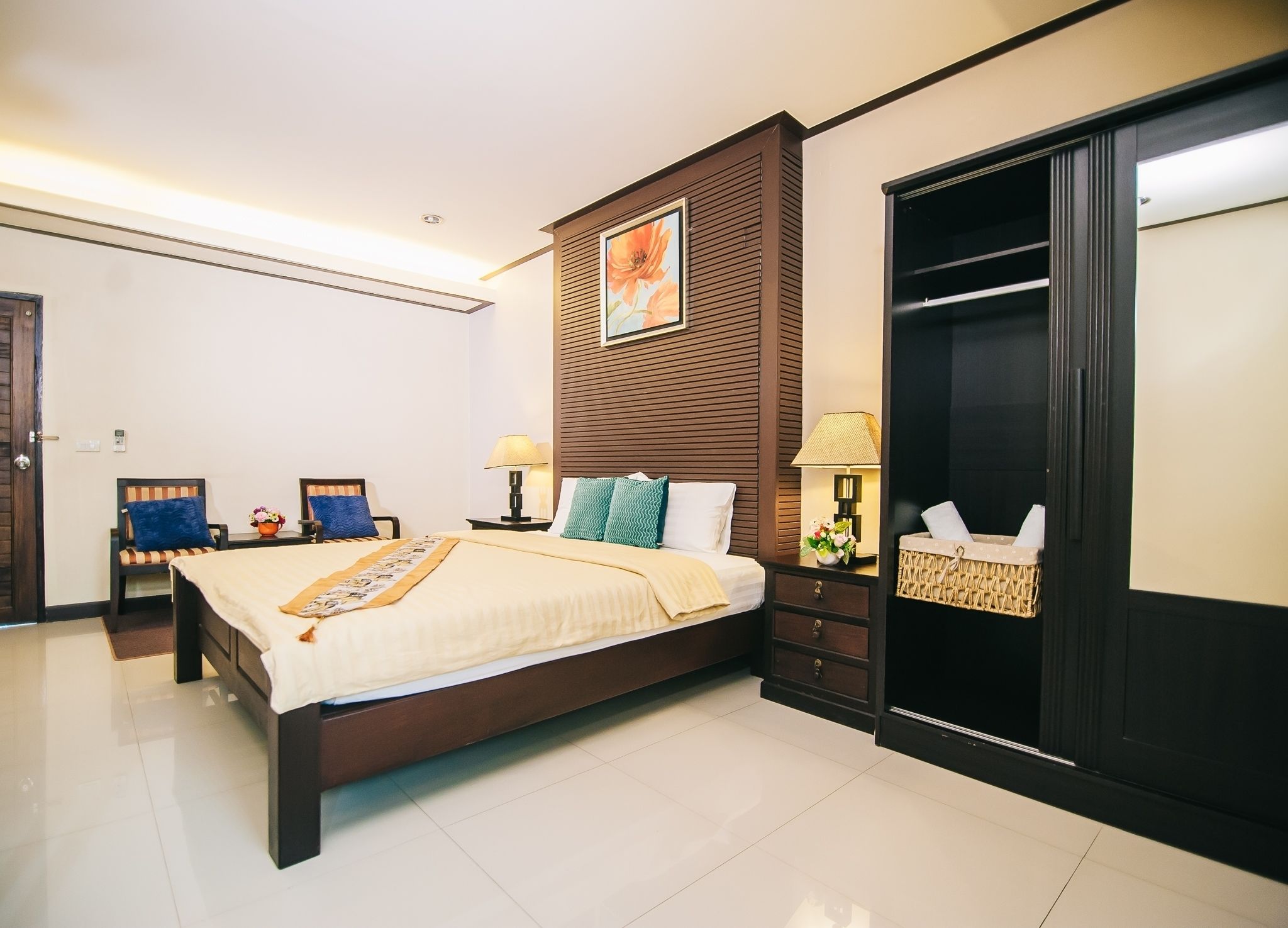 A hotel room with a large bed, a wooden headboard, a wardrobe, and a small seating area with chairs.