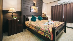 Habitación de hotel con cabecera de madera, cama con colcha estampada, dos mesitas de noche con lámparas y un equipo de aire acondicionado en la pared.