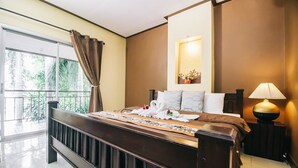 Habitación de hotel con una cama grande, una mesita de noche con lámpara, una ventana con cortinas y vistas al exterior con vegetación.