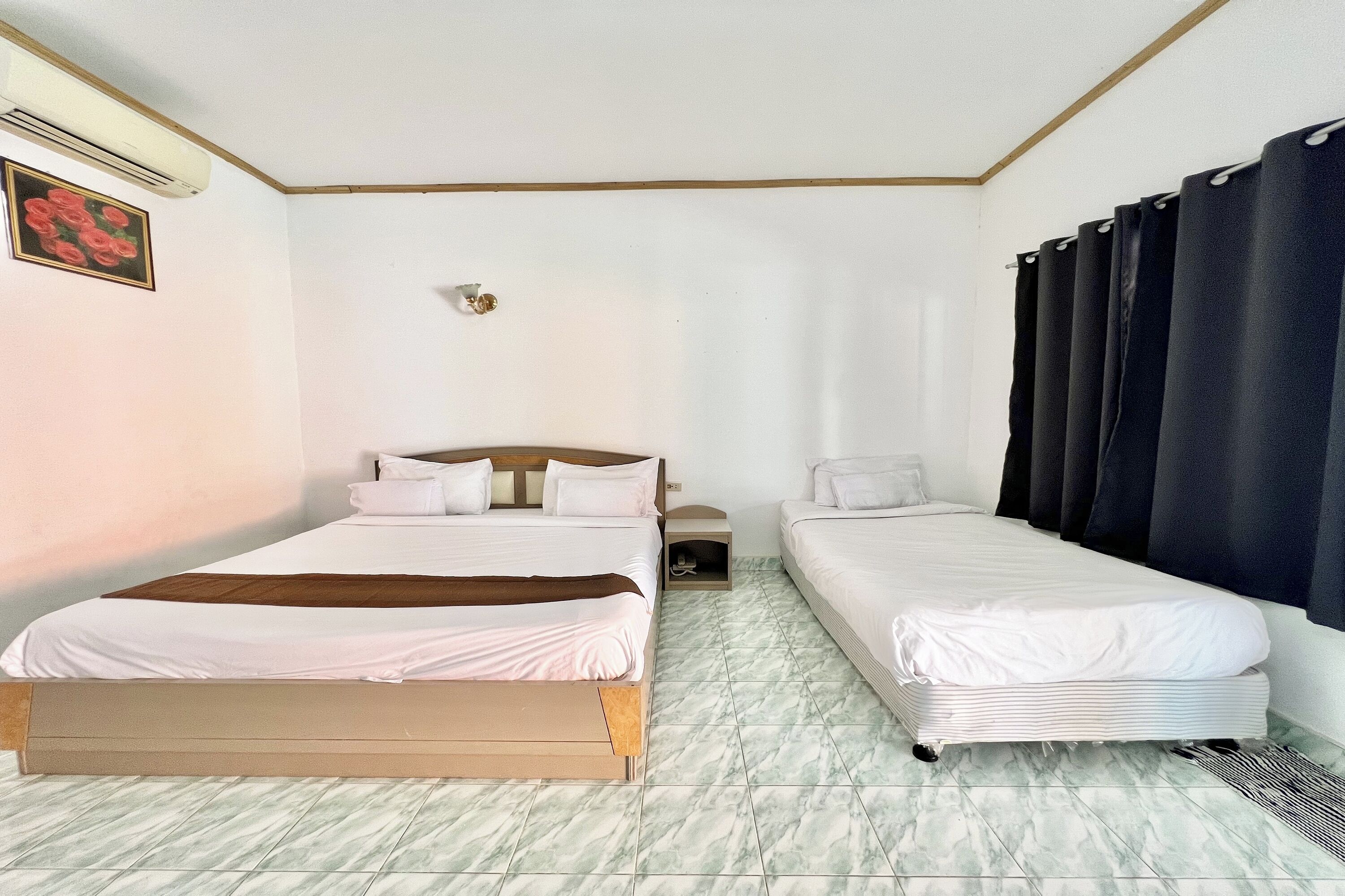 A hotel room with two beds, a small bedside table, a wall-mounted air conditioner, and a picture of roses.
