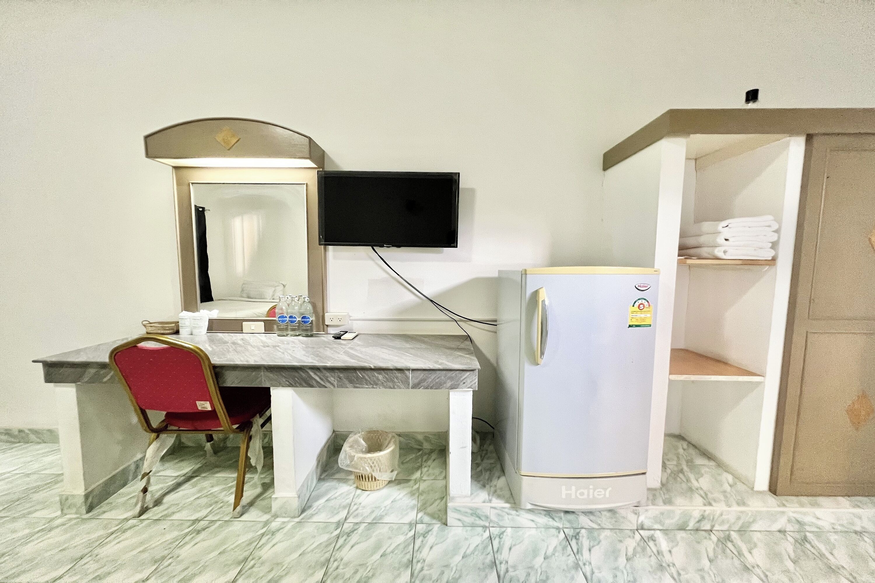 Una habitación de hotel con suelo de baldosas de mármol, un escritorio con una silla, un televisor montado en la pared y un refrigerador.