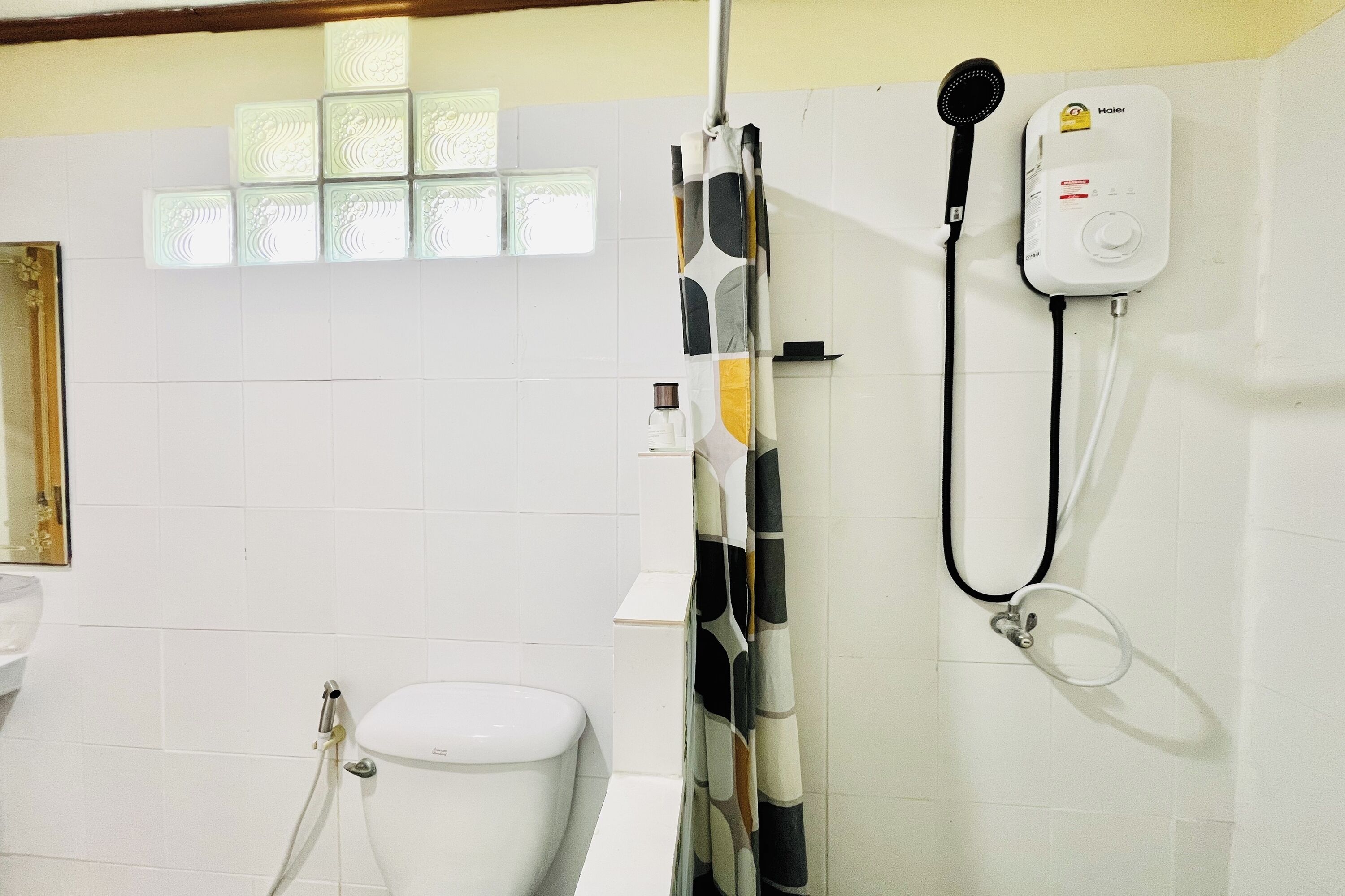 Un baño con inodoro, ducha con cortina y calentador en la pared.