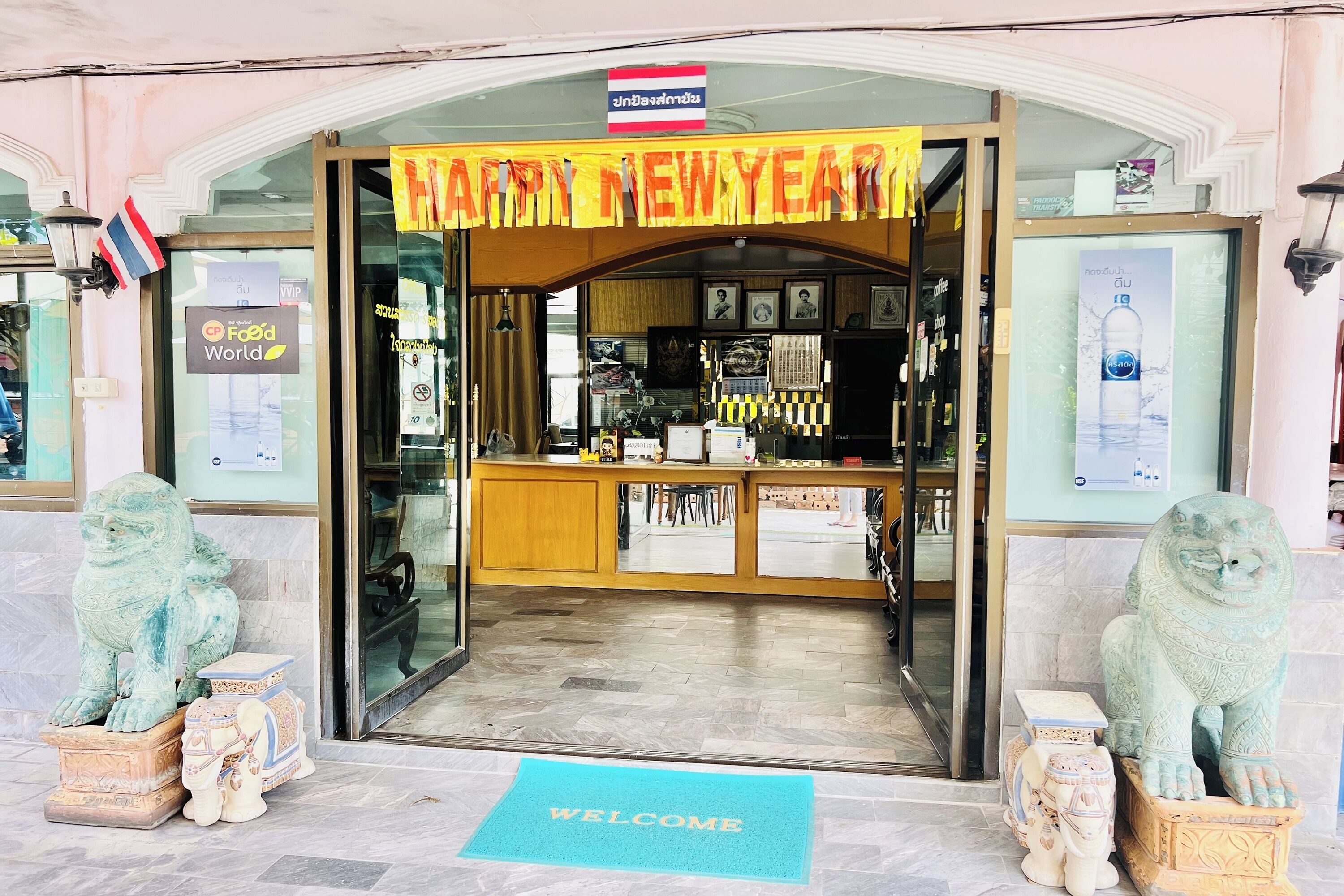 A New Year greeting at a shop entrance with a 'Food World' sign, a 'Welcome' mat, and two lion statues.