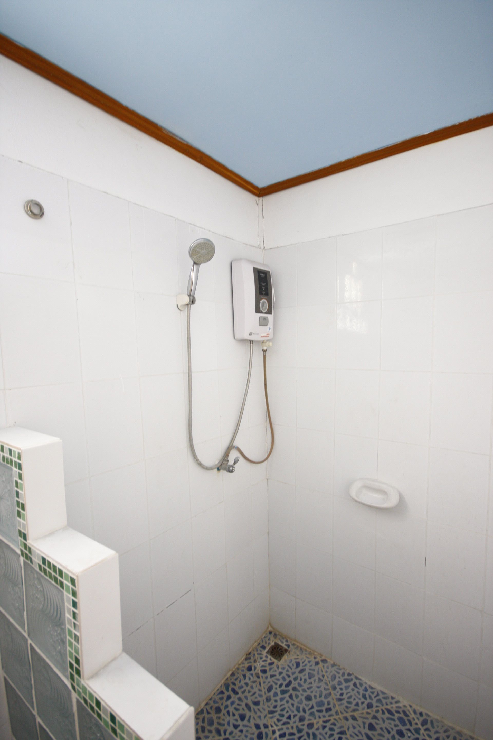 A small, tiled shower area with a handheld showerhead and a wall-mounted control panel.