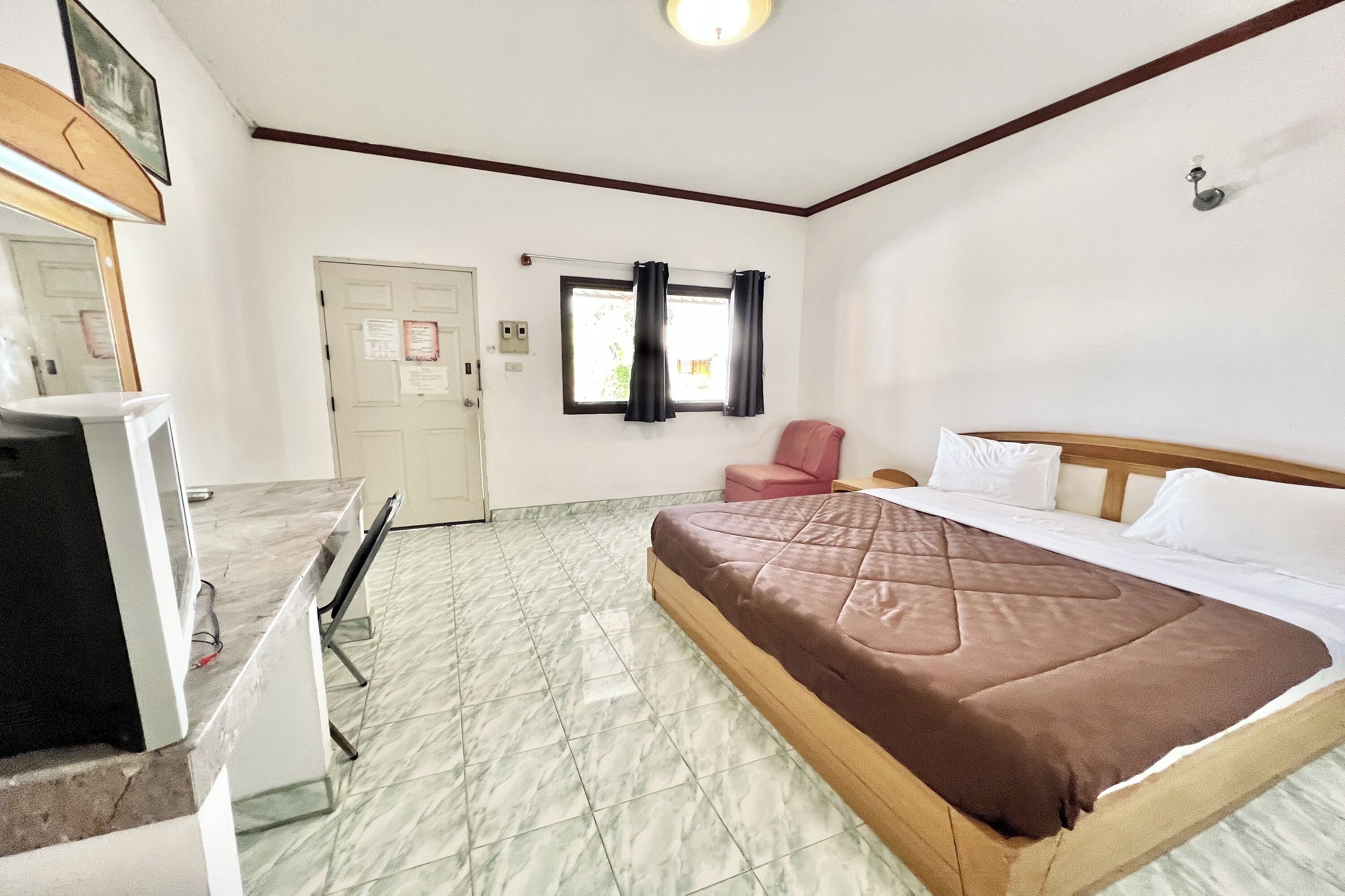 A hotel room with a bed, a desk with a chair, a window with curtains, and a door.