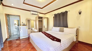 Une chambre d’hôtel avec un grand lit, une armoire, une salle de bain avec un lavabo et un miroir, et un ventilateur de plafond.