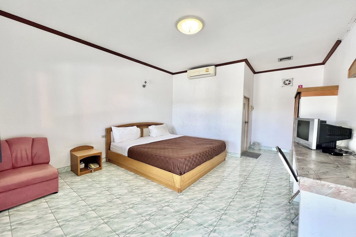 Ein Schlafzimmer mit einem Bett, einem roten Sofa, einem kleinen Nachttisch aus Holz, einem Fernseher und einer Mikrowelle.