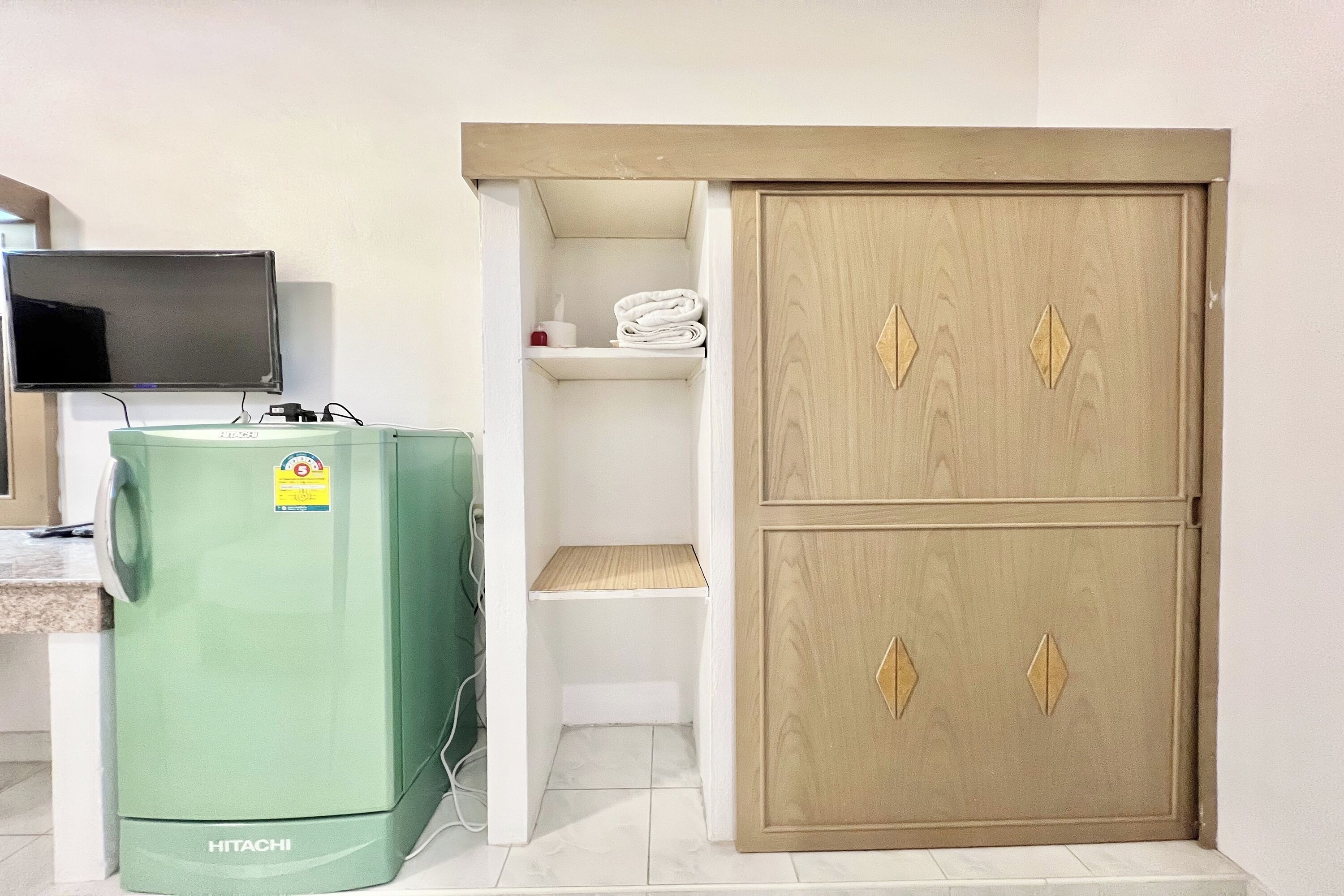 Ein Zimmer mit einem Hitachi-Warmwasserbereiter, einem Fernseher und einem zweitürigen Holzschrank.