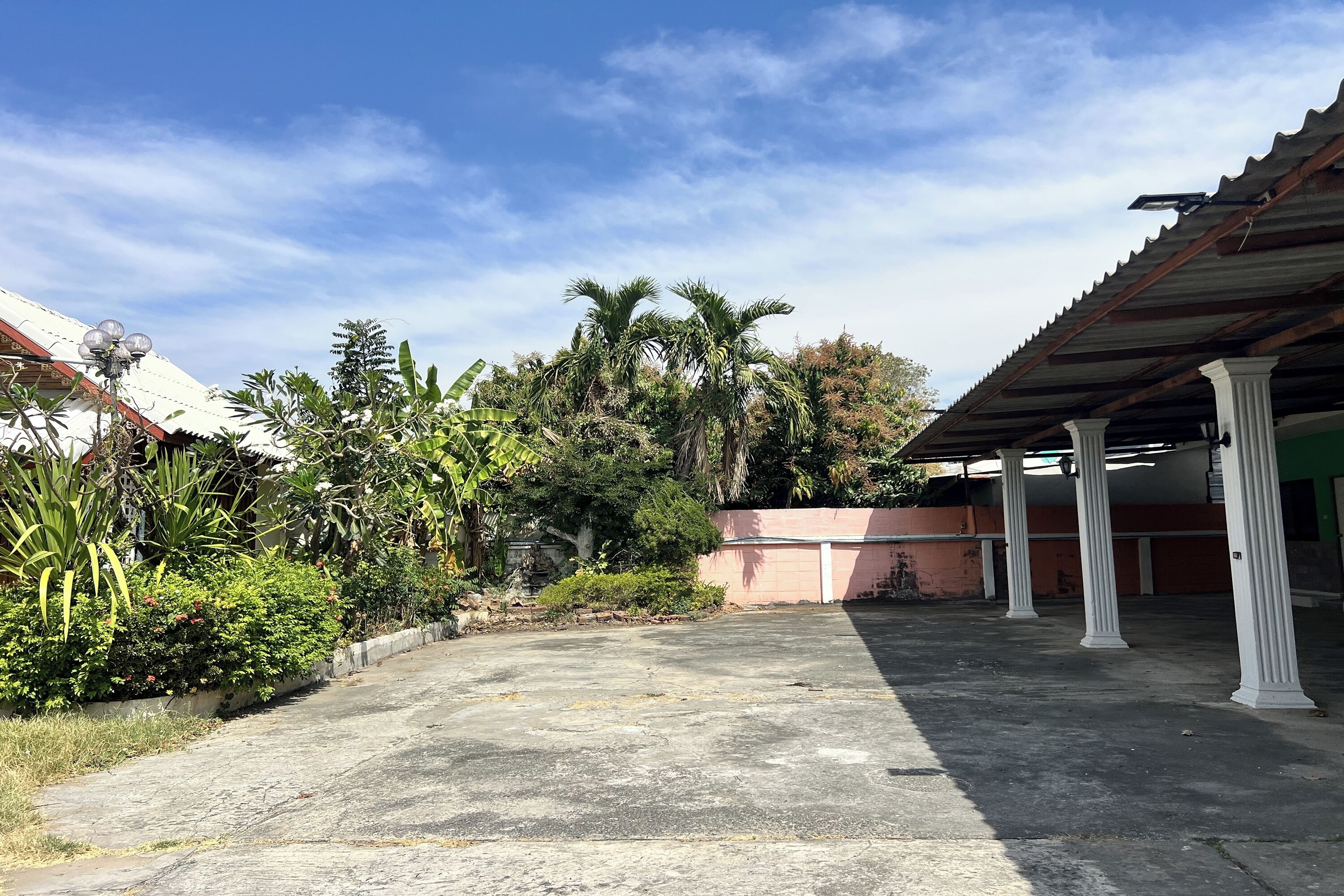 Un espacio al aire libre techado con piso de concreto, rodeado de follaje y palmeras.