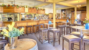 Zona de bar con taburetes de madera, barra y una variedad de botellas y vasos.