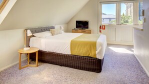 Un dormitorio con cama, mesita de noche, lámpara, televisor y ventana con vista a edificios.