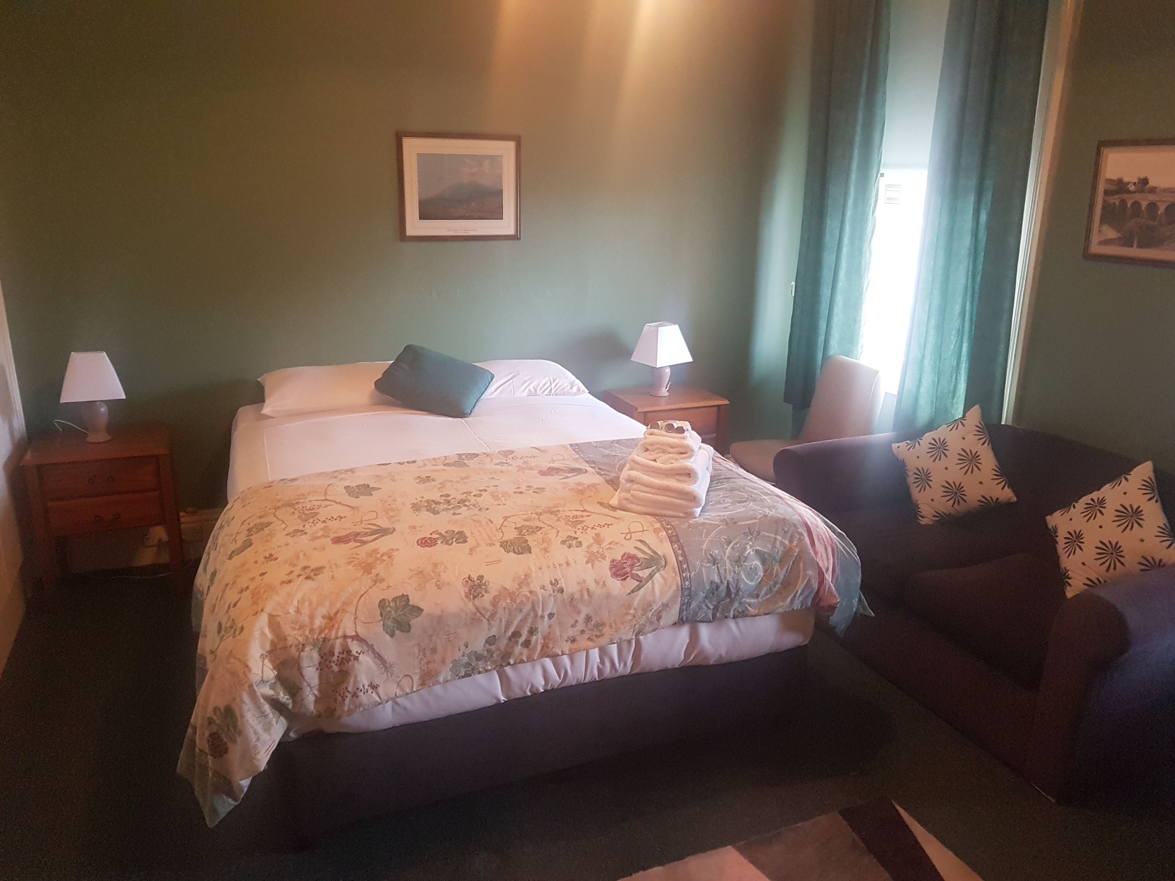 Ein Hotelzimmer mit einem Bett, zwei Nachttischen, einem Sofa und einem Fenster mit Vorhängen.