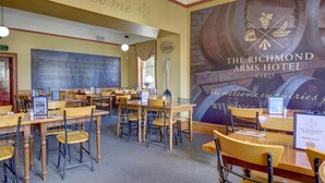 Un comedor con varias mesas y sillas de madera, una pizarra con escritura y un mural grande de barriles de vino.