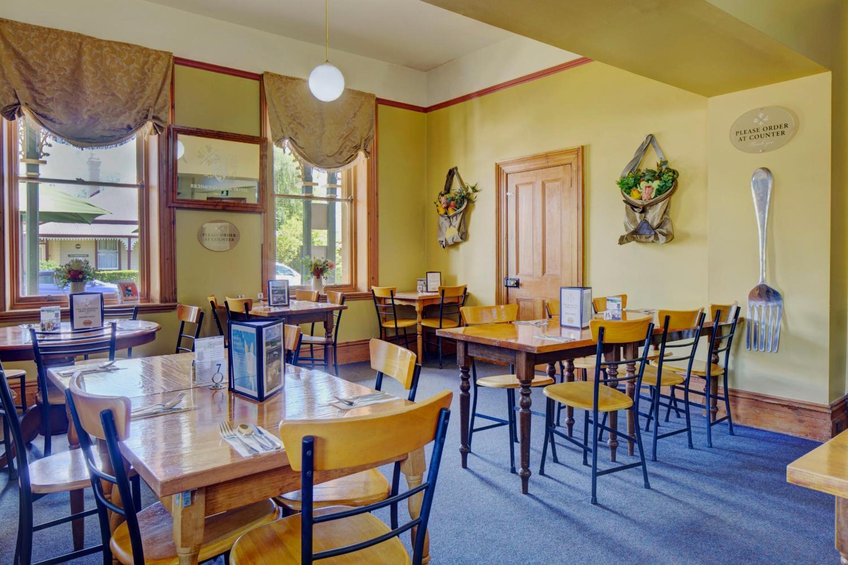 En restaurant med træborde og stole, et skilt der viser, at man bestiller i skranken, og et vindue med udsigt udad.