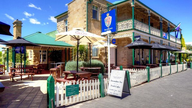 Un edificio histórico con techo verde, asientos exteriores y un letrero que dice 'Richmond Arms Hotel'.