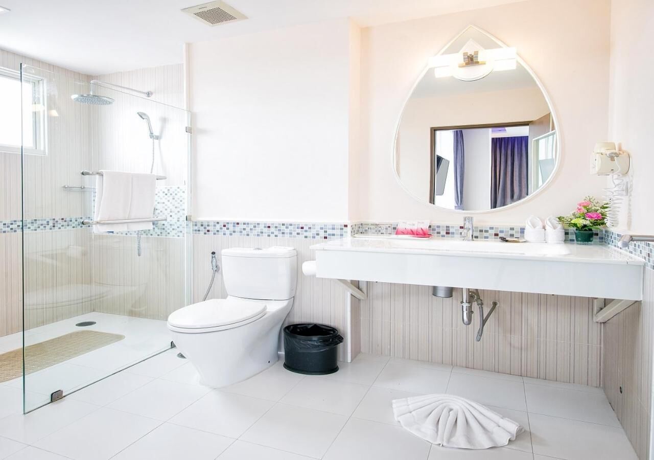 A modern bathroom with a glass-enclosed shower, a white toilet, a sink with a mirror above it, and a tiled backsplash.