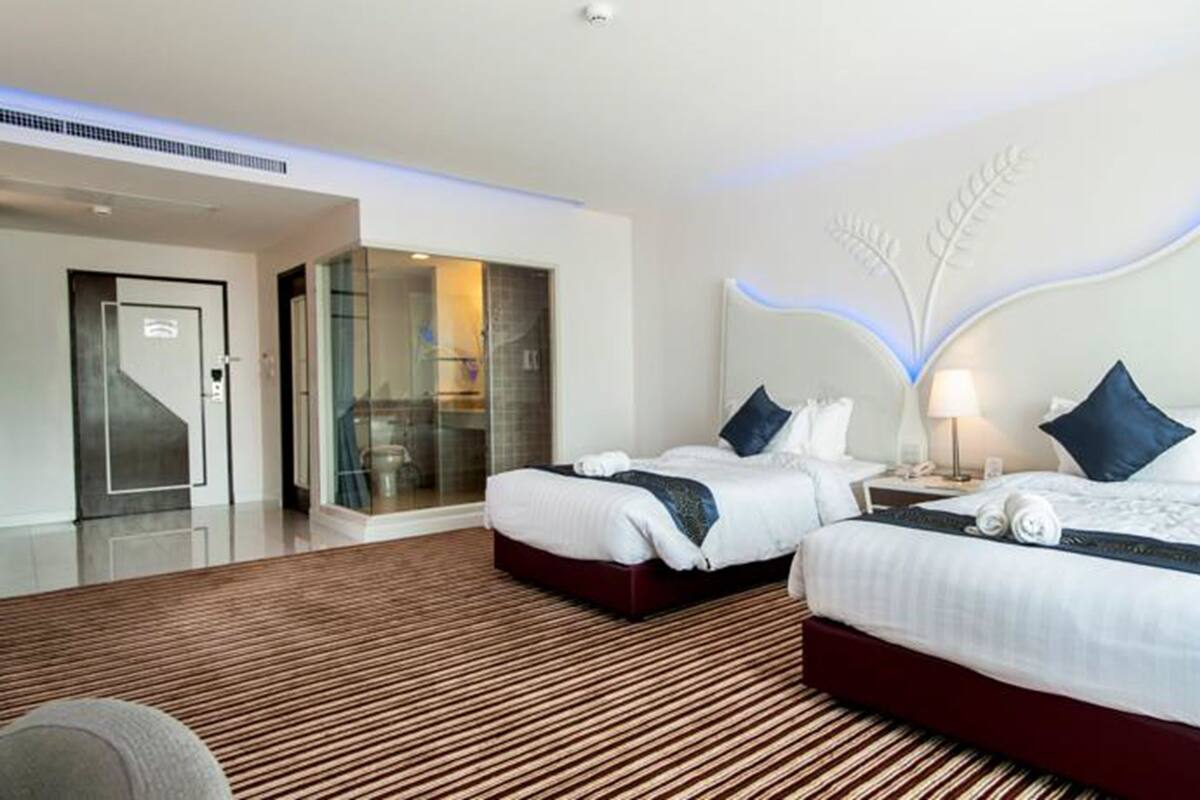 A modern hotel room with two beds, a glass shower enclosure, and a wooden floor.