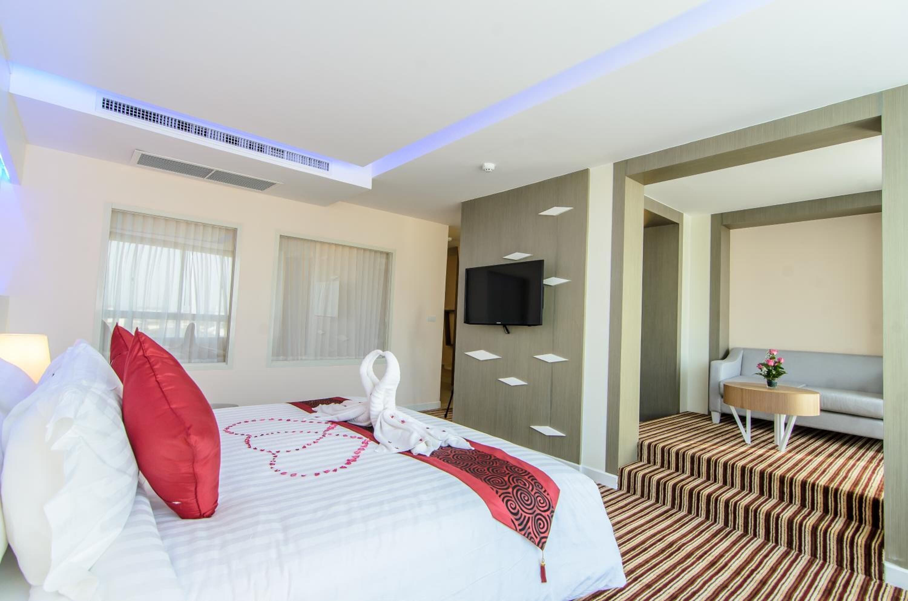 Une chambre d’hôtel avec un lit bien fait, un téléviseur à écran plat fixé au mur, un canapé et une moquette à motifs.