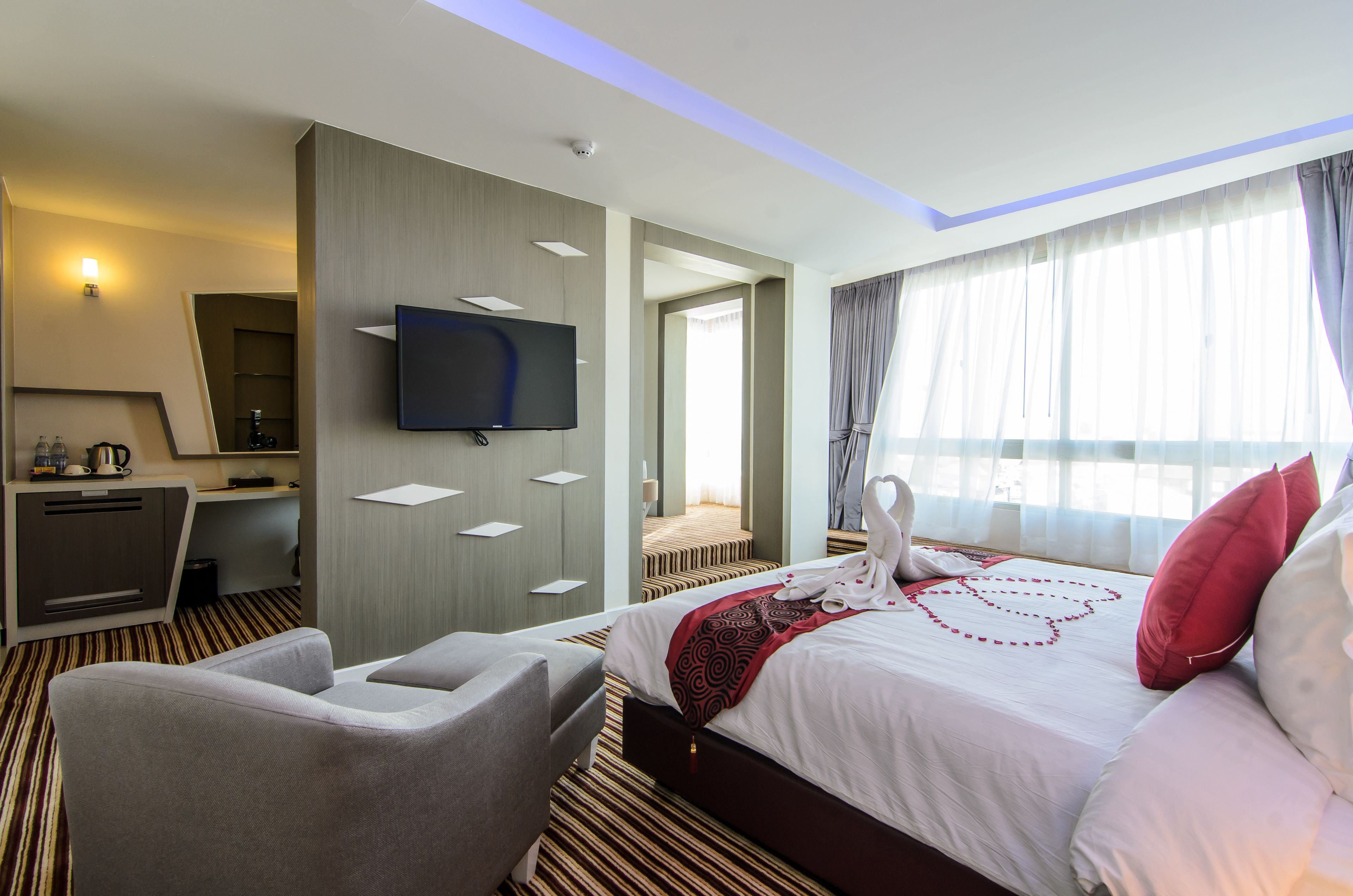 A hotel room with a bed, a desk, a TV, and a seating area.