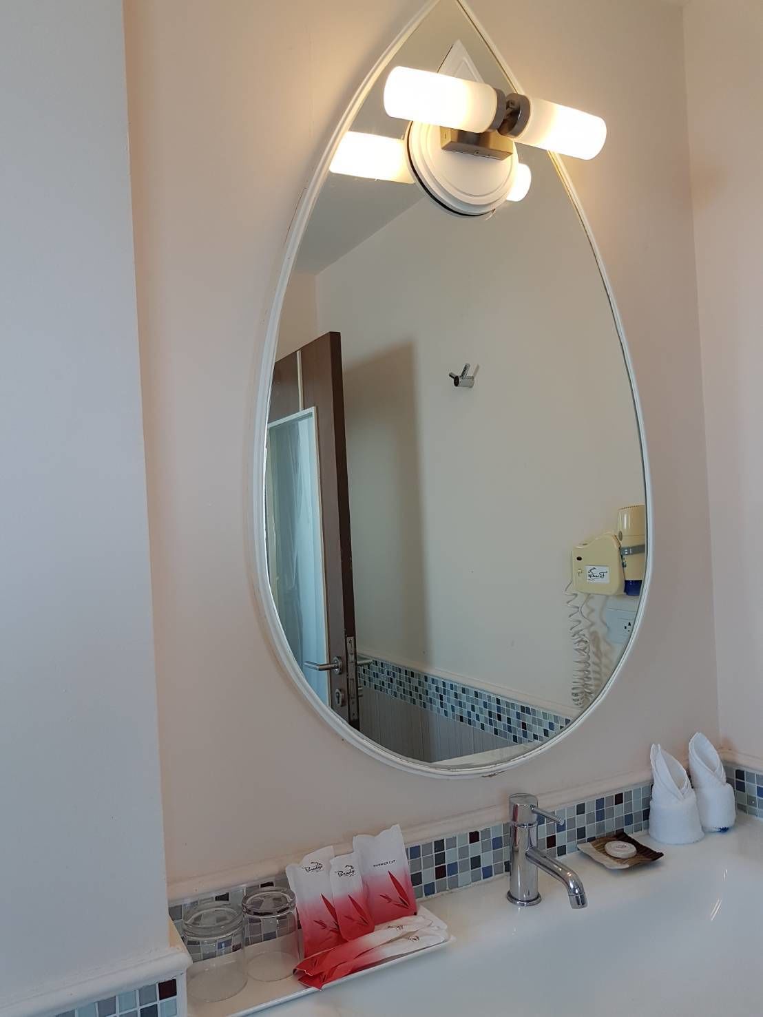 A bathroom with a large oval mirror, a white sink, a towel rack, and a soap dispenser.