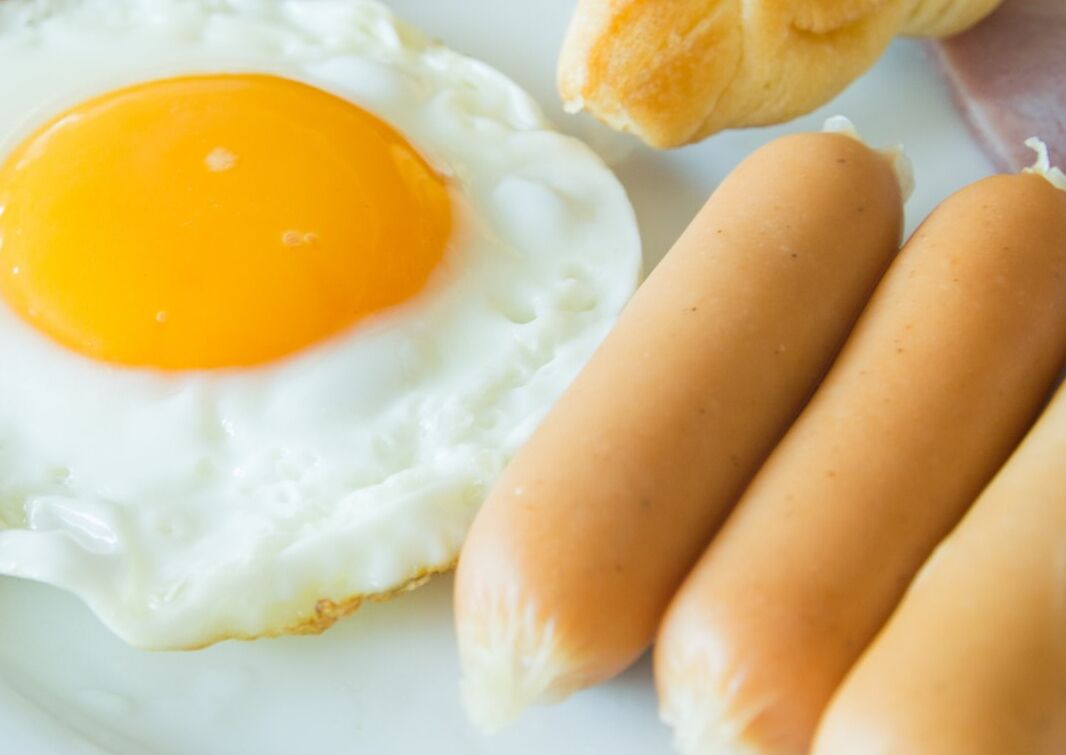 A breakfast plate with a fried egg, two sausages, and a piece of toast.