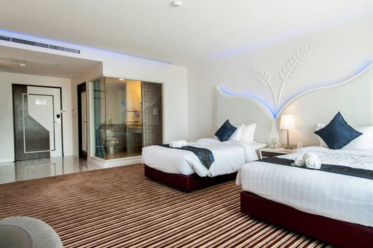 A hotel room with two beds, a glass-enclosed shower, a wooden floor, and a modern design.