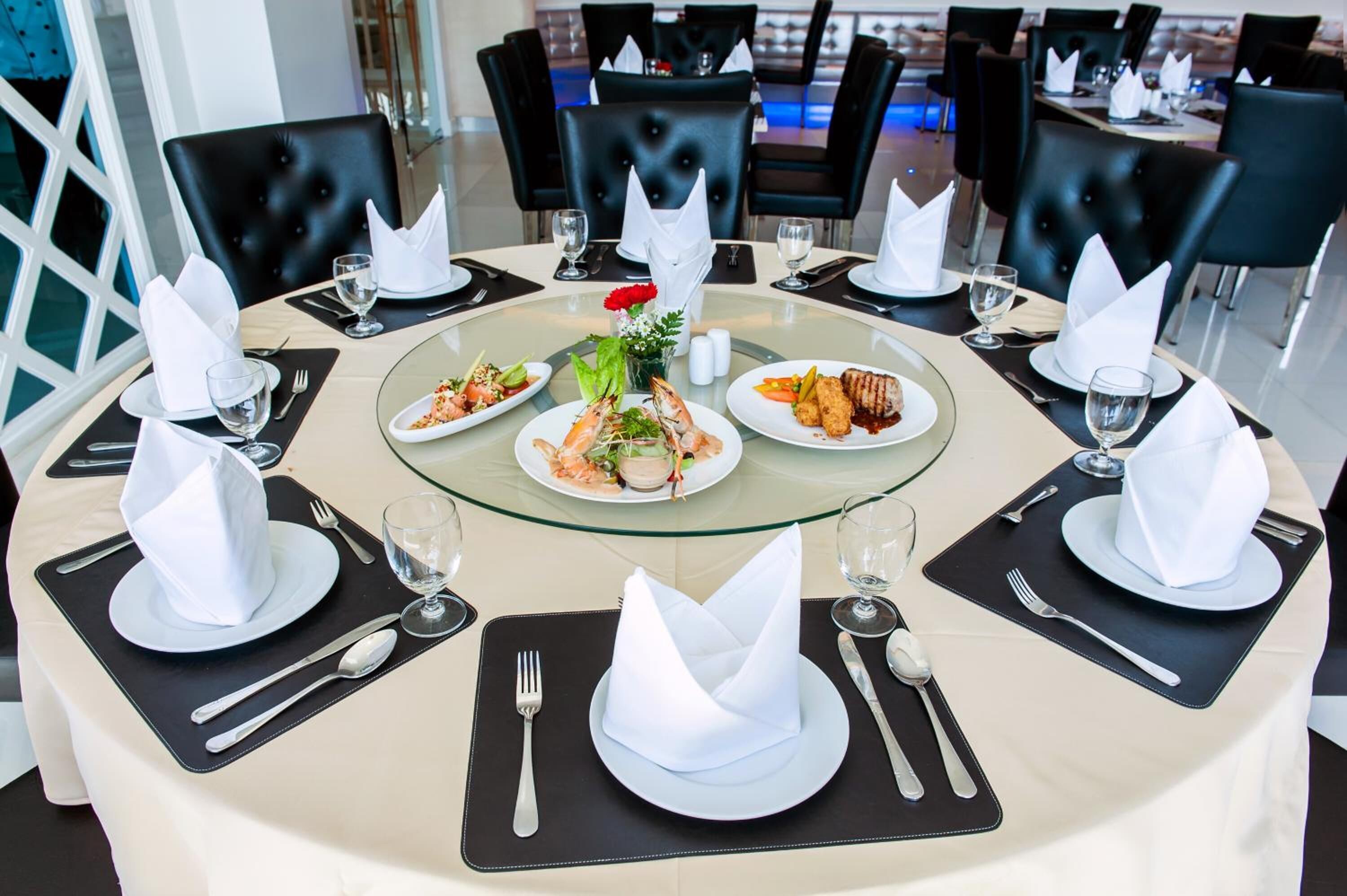 A round dining table with black chairs, white napkins, and a glass centerpiece.