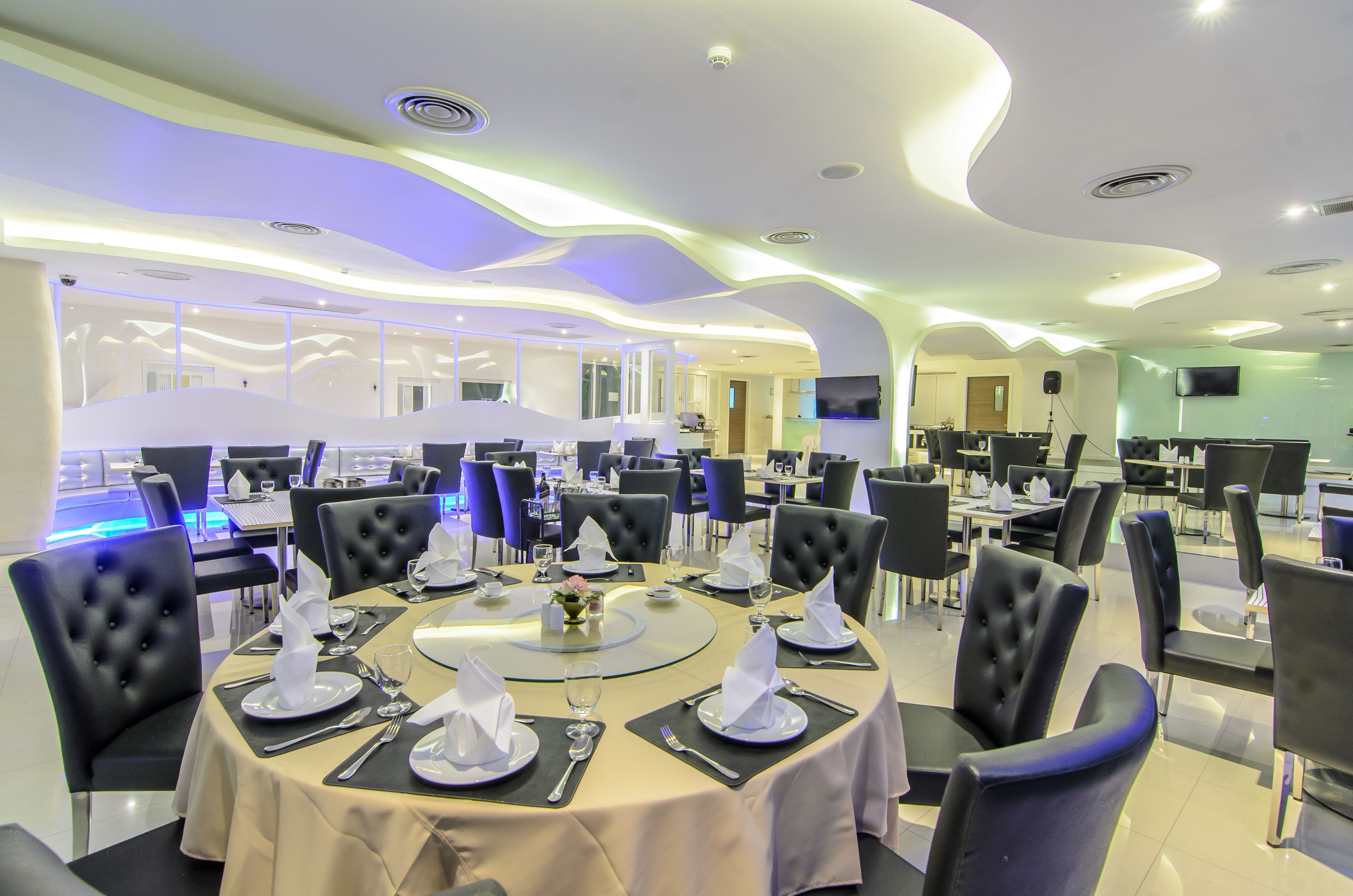 A modern dining area with round tables, black upholstered chairs, and a central decorative piece.