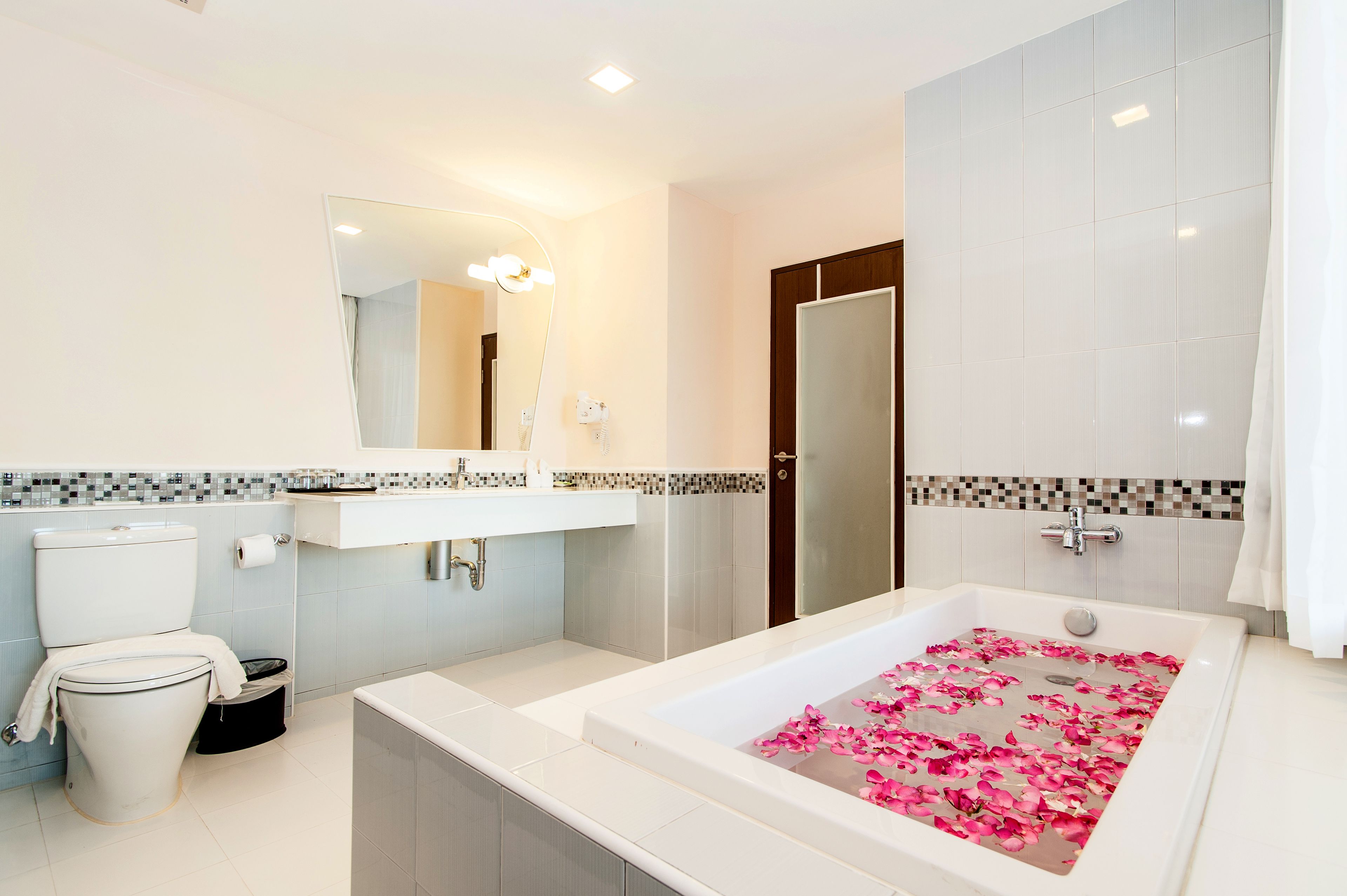 A modern bathroom with a toilet, sink, and bathtub with rose petals.