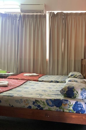 A room with two beds, a table, and an air conditioning unit.
