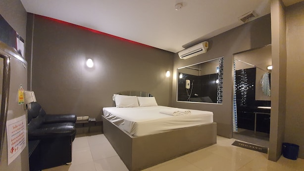 A modern bedroom with a large bed, a black leather chair, a bedside table, a mirror, and an air conditioning unit. - Heaven Inn (Si Racha)