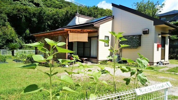Una casa moderna con un porche cubierto, un jardín y un letrero que indica un huerto.