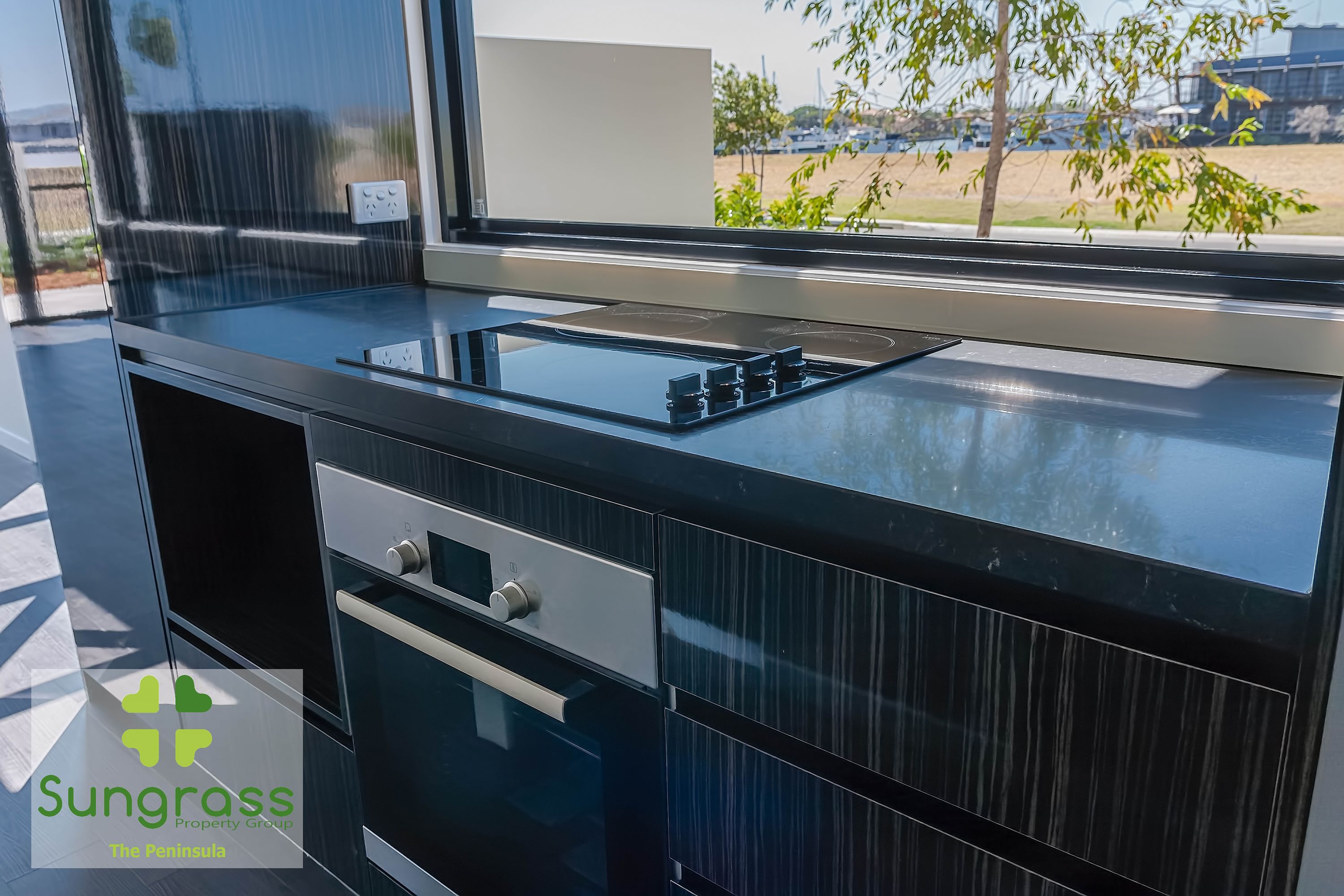 Una cocina moderna con horno empotrado, un lavamanos de acero inoxidable y ventana con vistas al exterior.