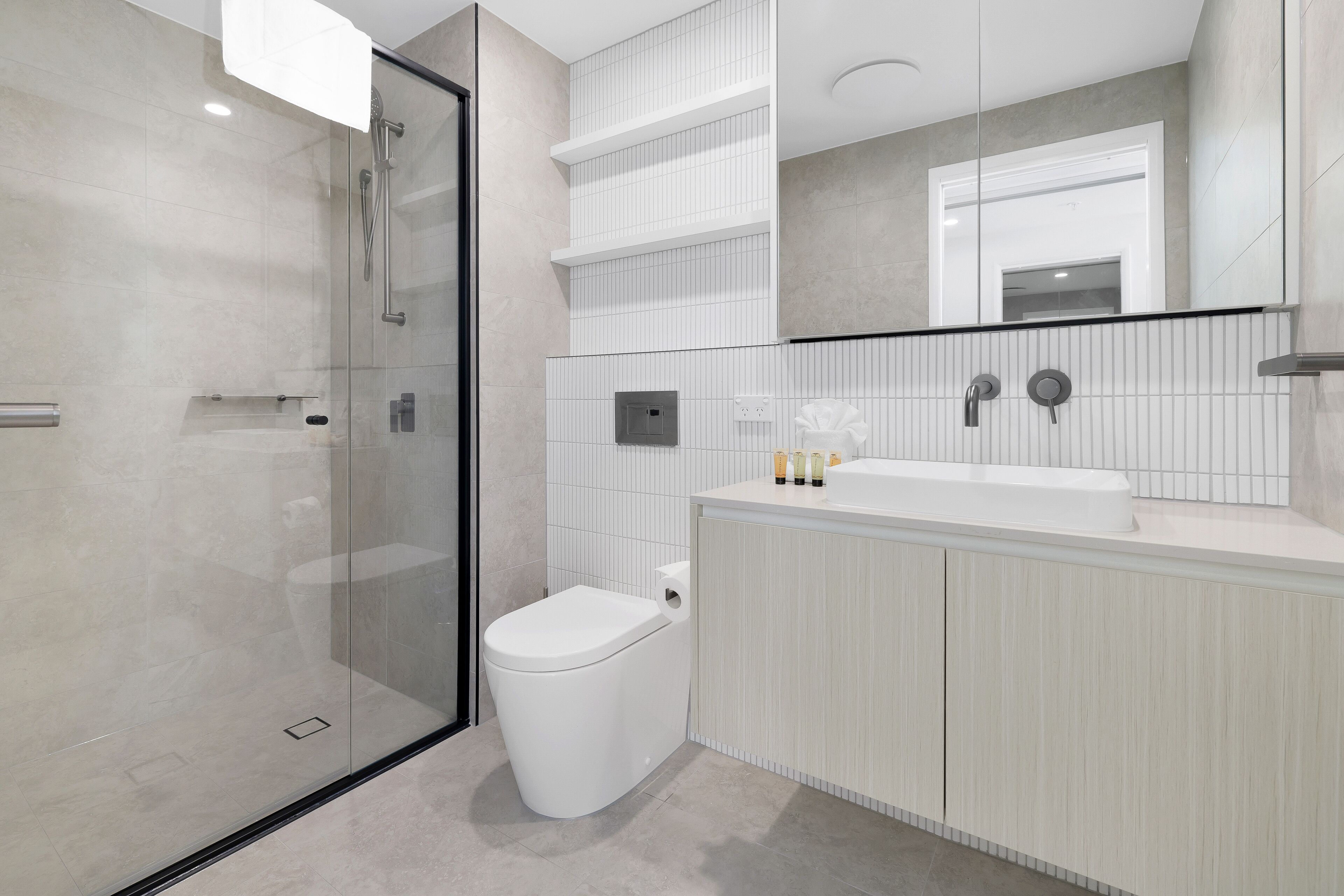 A modern bathroom with a glass-enclosed shower, a white toilet, and a vanity with a mirror.