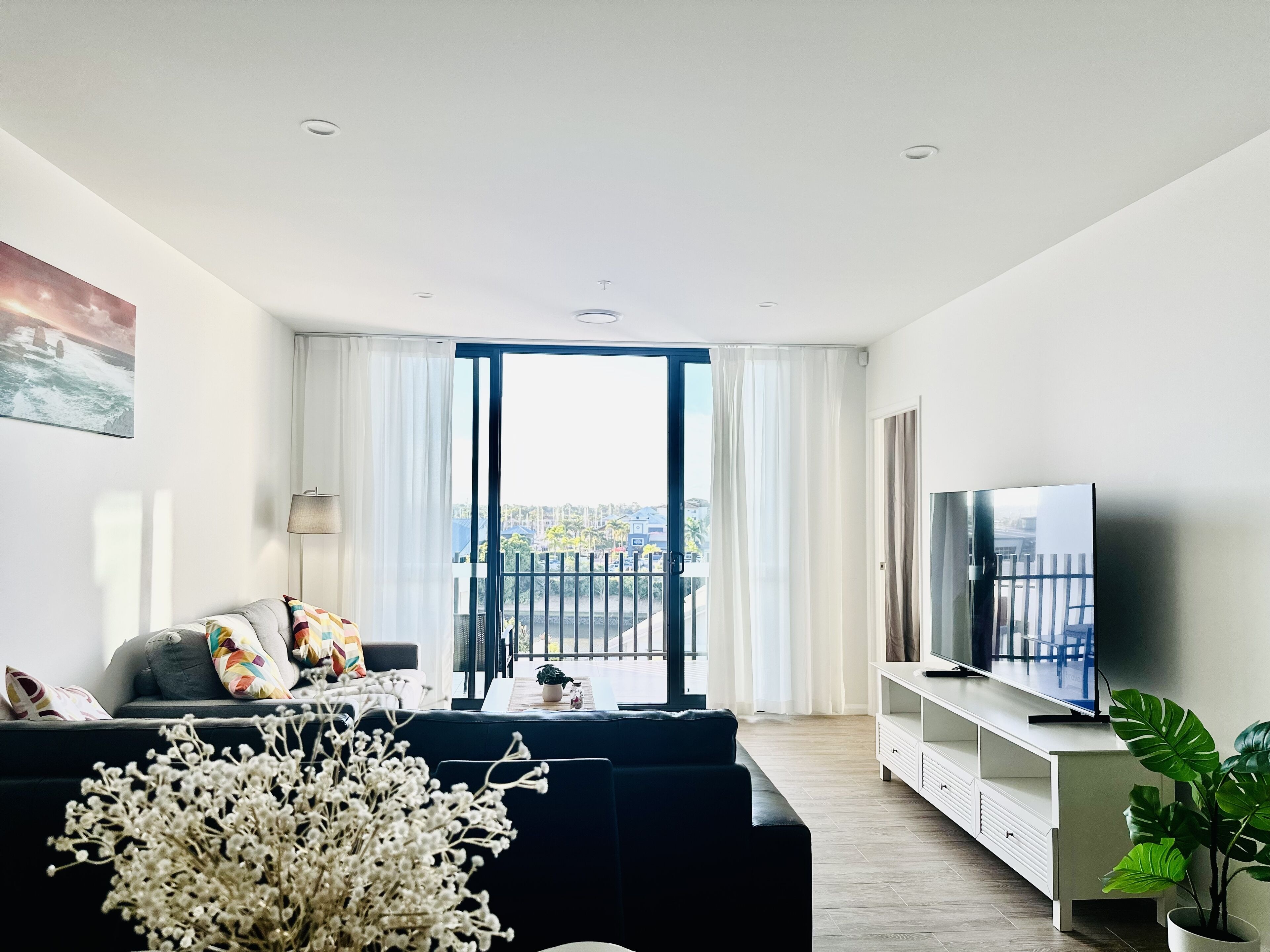 Una sala de estar moderna con un sofá, un televisor y un balcón con cortinas.