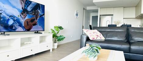 Una sala de estar moderna con un televisor de pantalla plana, un sofá de cuero, una mesa de centro con revistas y una planta en maceta.