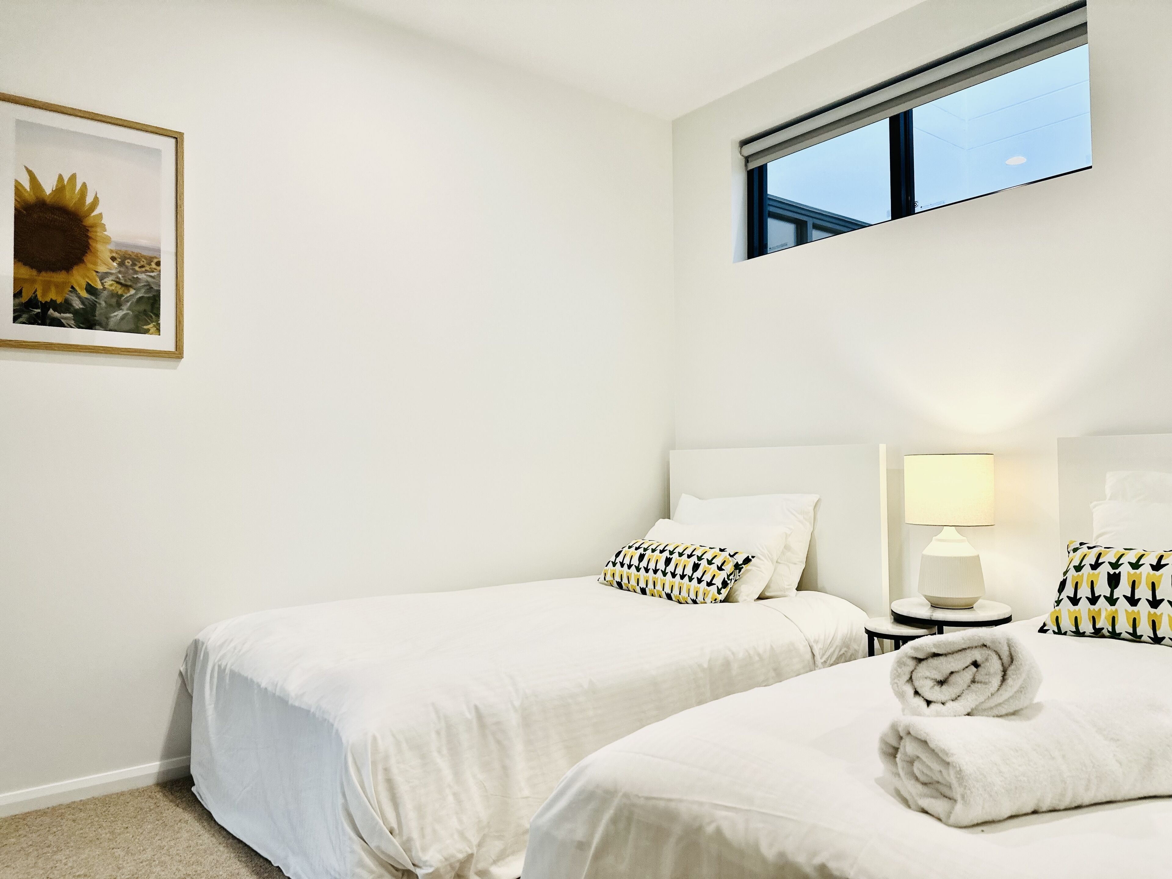 Une chambre d’hôtel avec deux lits, une fenêtre, un tableau représentant un tournesol et une lampe sur la table de chevet.