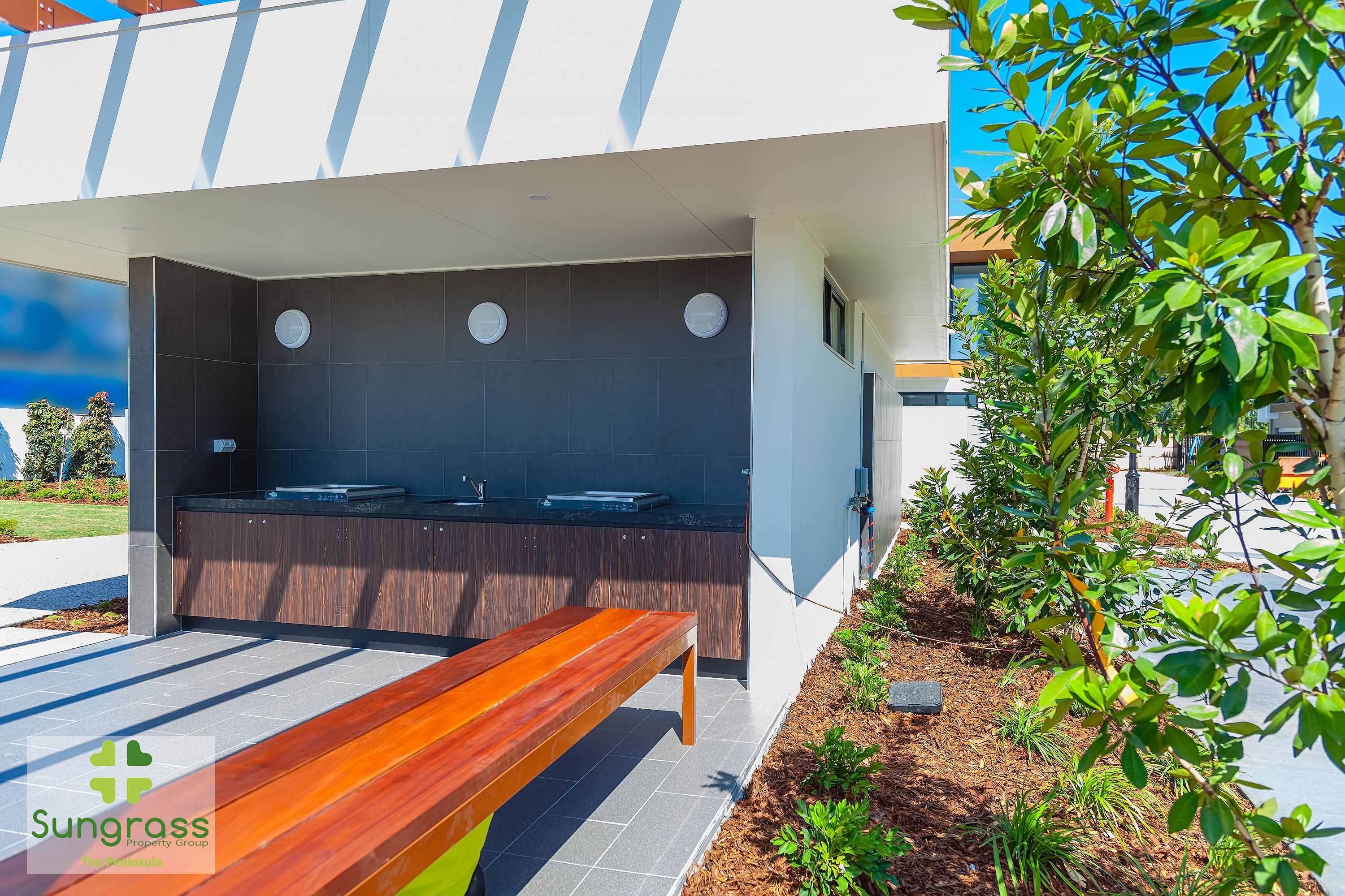 A modern outdoor area with a wooden bench, a built-in kitchen counter, and a small garden with plants.