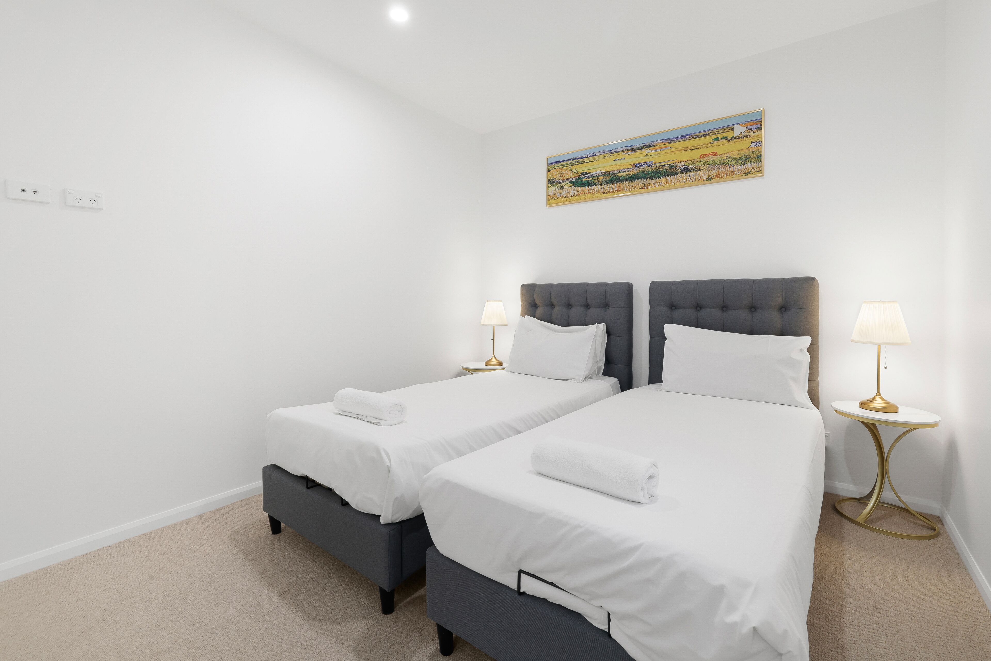 A hotel room with two beds, a painting on the wall, and a small round table with a lamp.