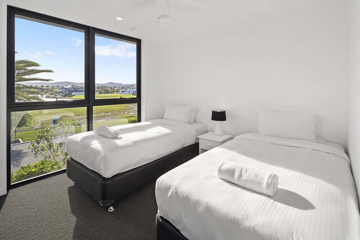 A hotel room with two beds, a large window with a view of the landscape, and a nightstand with a lamp.