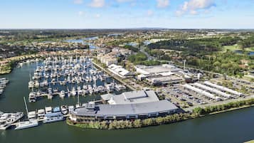 A marina with numerous boats docked, a large building with a flat roof, and a parking area with several cars.