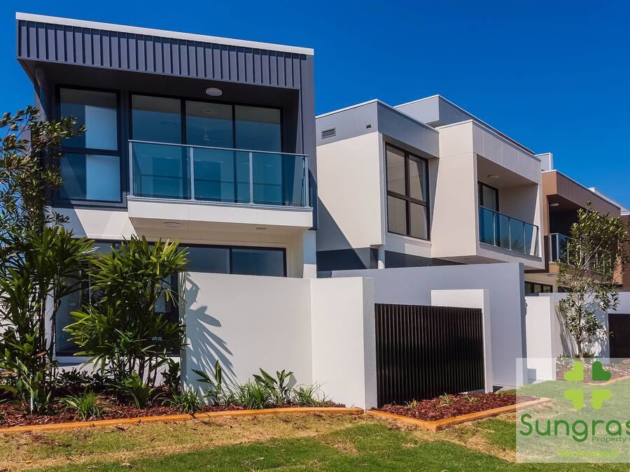 A modern two-story residential building with large windows, a balcony, and a well-maintained garden.