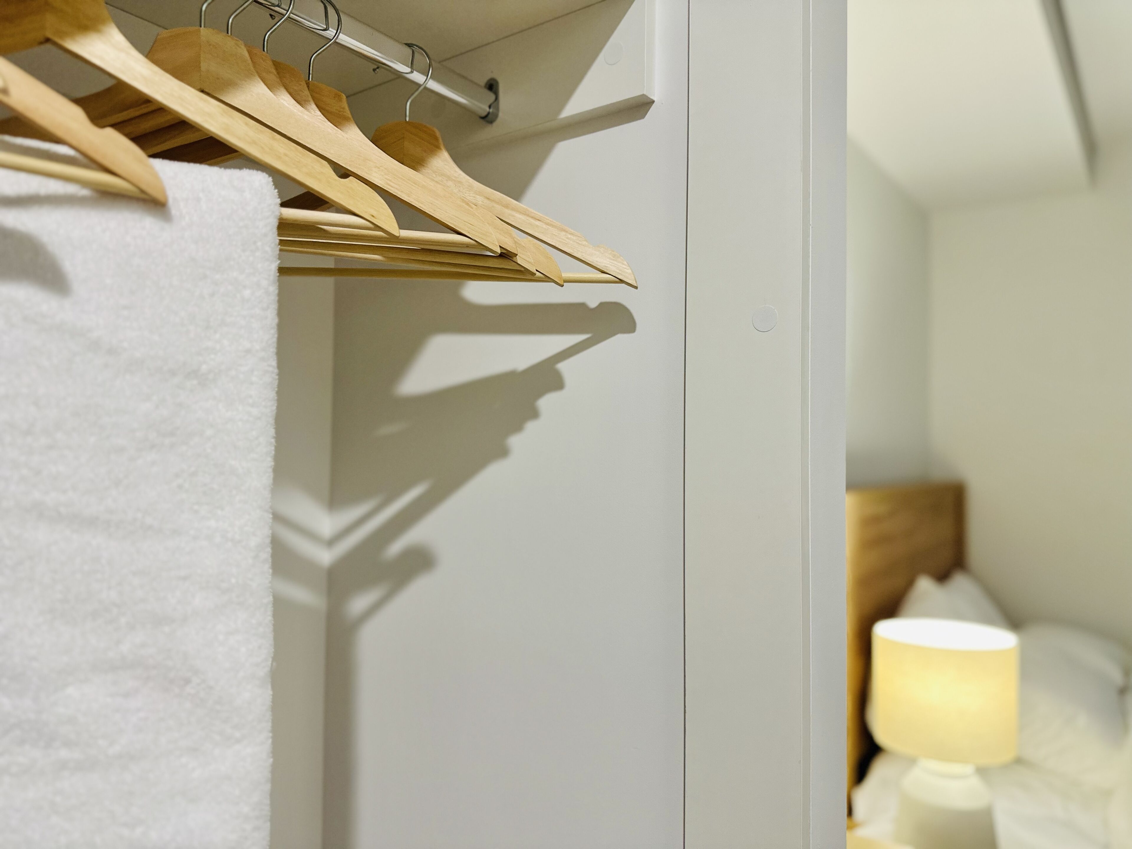 A white wardrobe with wooden hangers and a white towel.