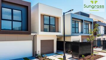 A modern residential building with a garage, a black fence, and a small tree in the front yard.