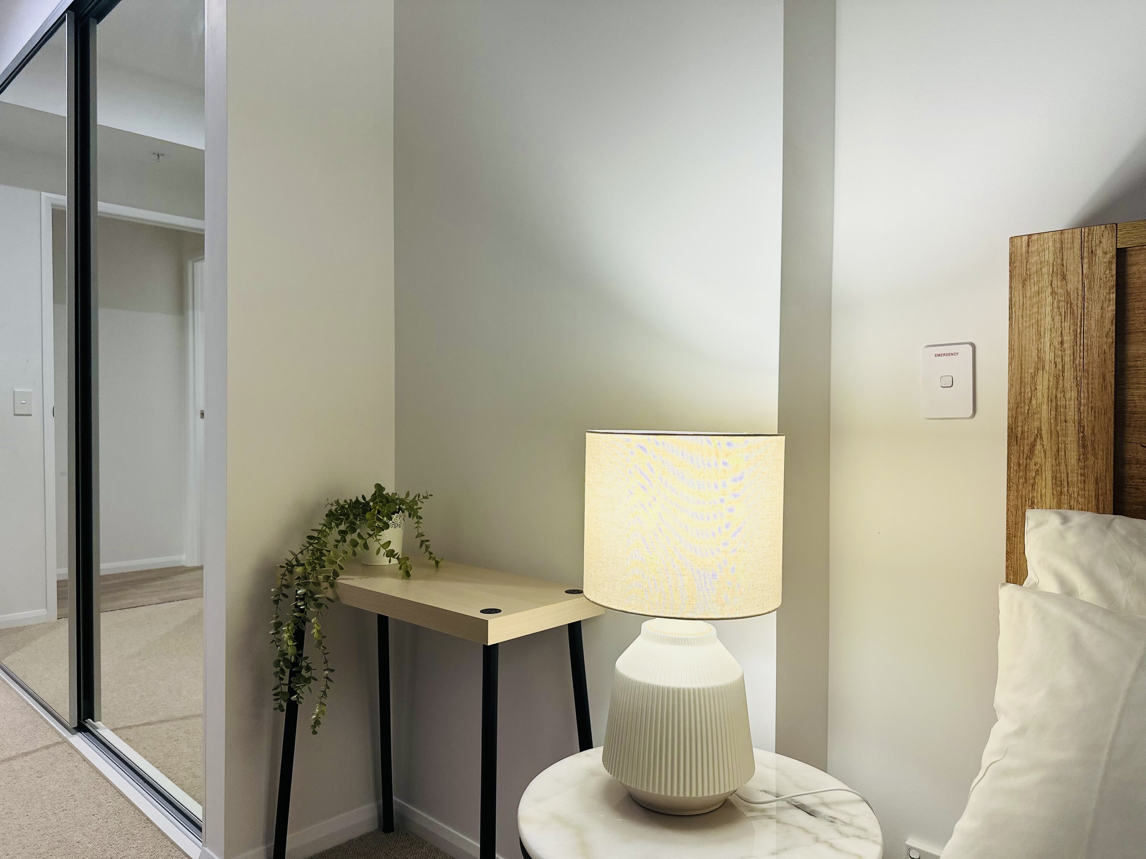 A corner room with a lamp on a small table, a potted plant, and a view through a glass door.