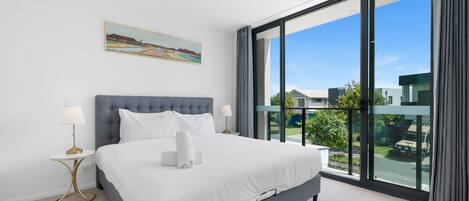 Une chambre d’hôtel moderne avec un grand lit, deux tables de chevet, un tableau au mur et un balcon offrant une vue sur la ville.