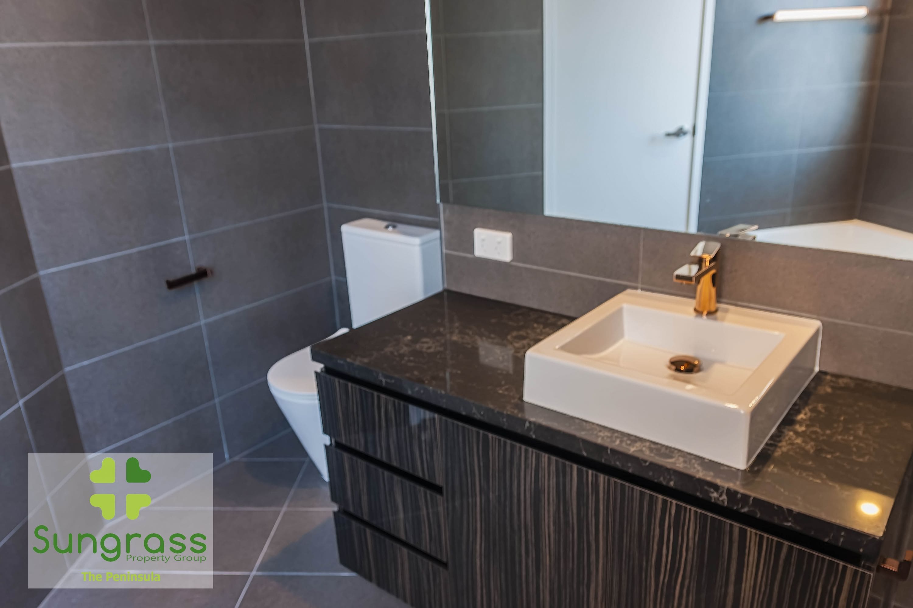 Un baño moderno con encimera de mármol oscuro, un lavabo blanco y un espejo grande.